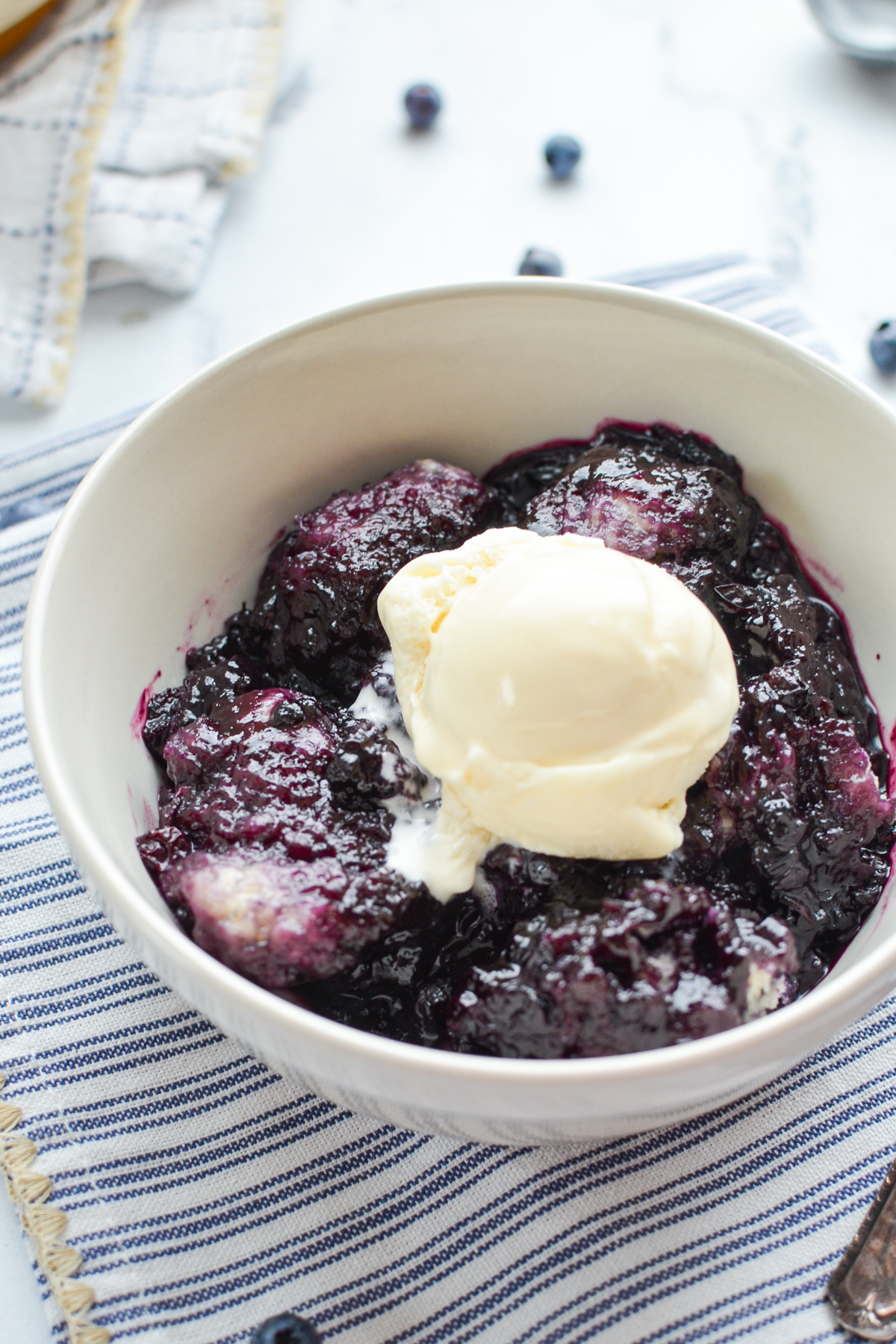 A bowl of blueberry grunt topped with a scoop of ice cream.