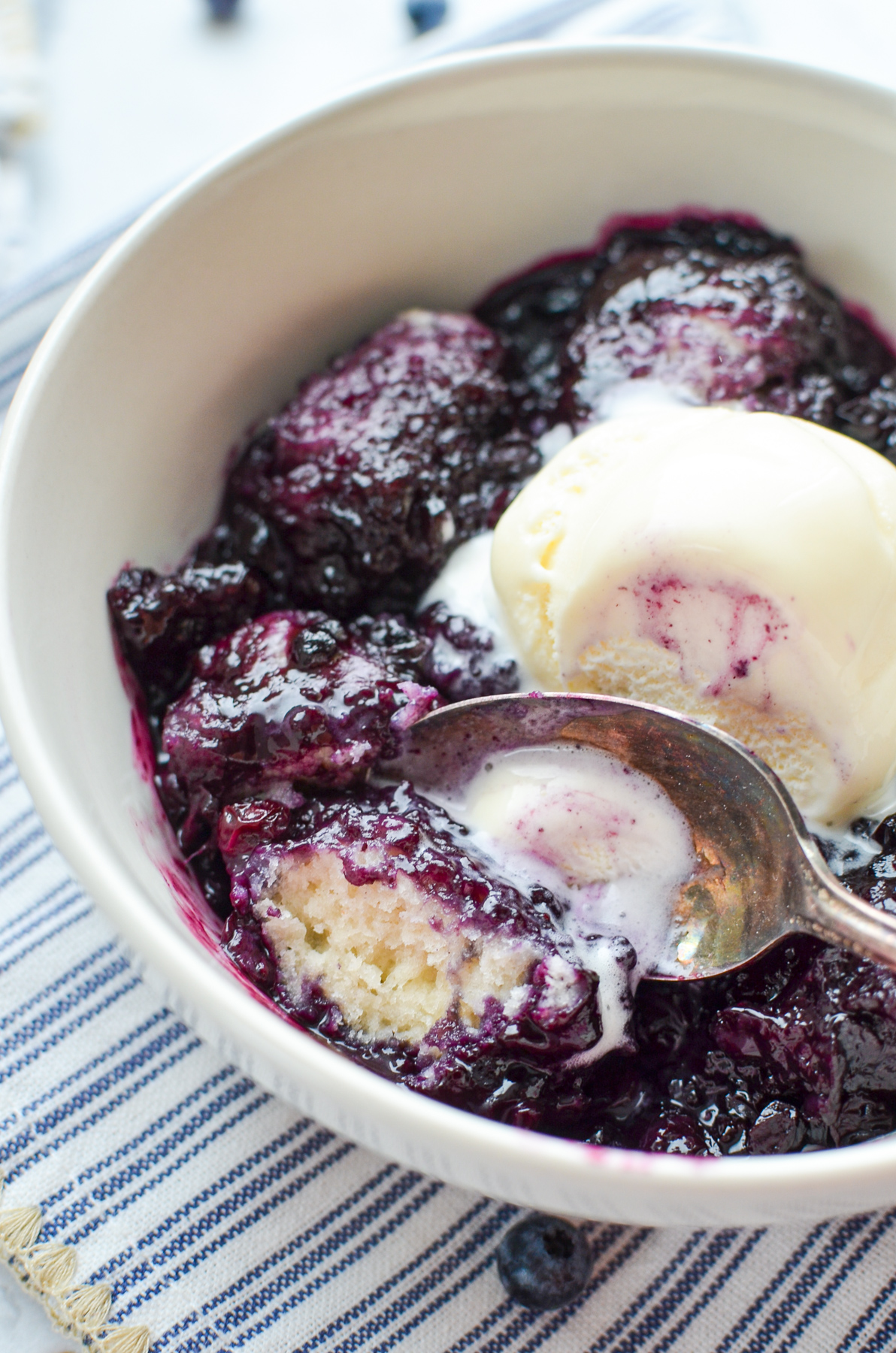 A bowl of stewed blueberries with biscuit dough and scoop of ice cream.