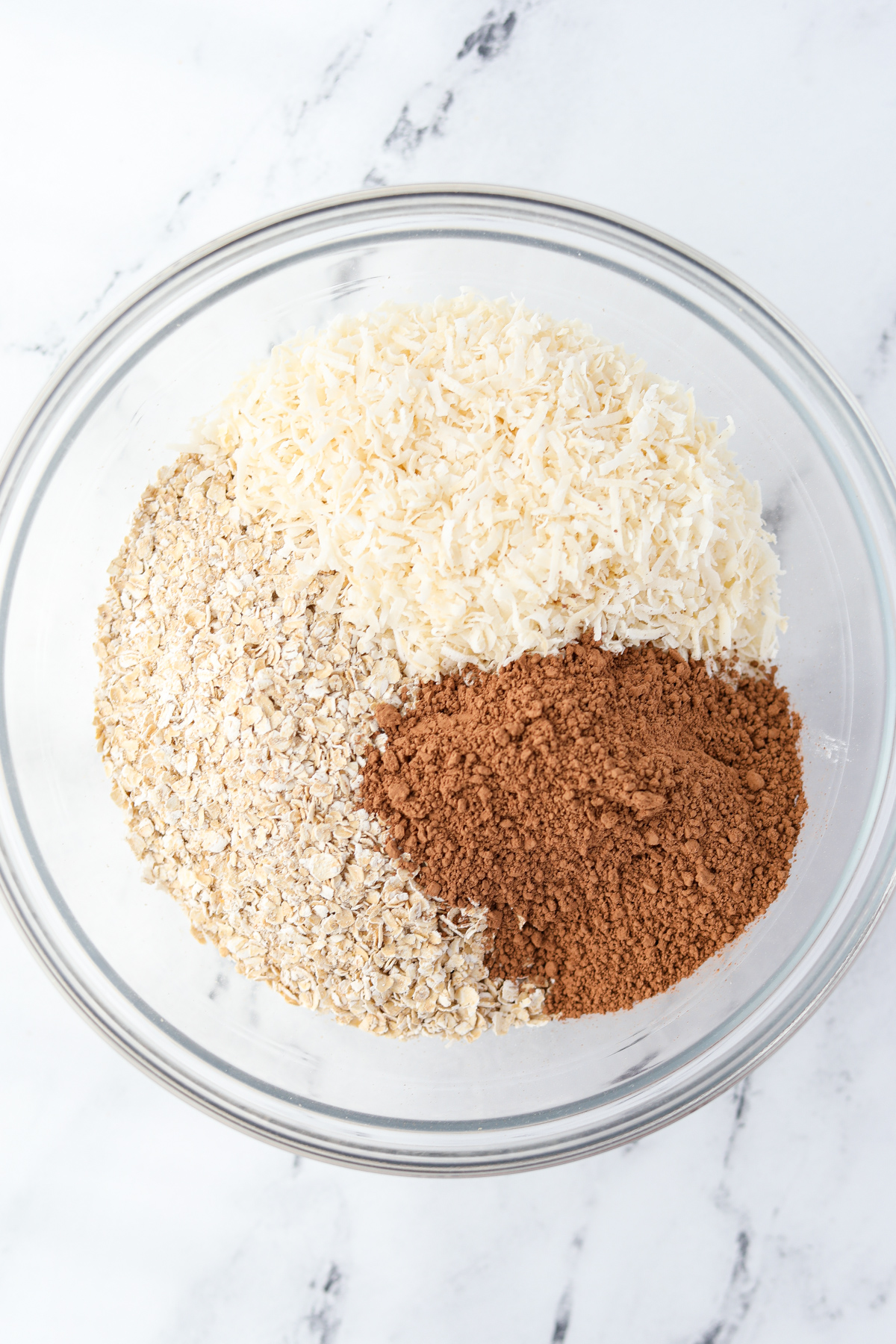 A bowl of oats, coconut, and cocoa powder ready to be mixed together.