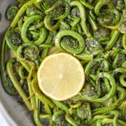 Fiddleheads cooked in a skillet with a lemon slice.