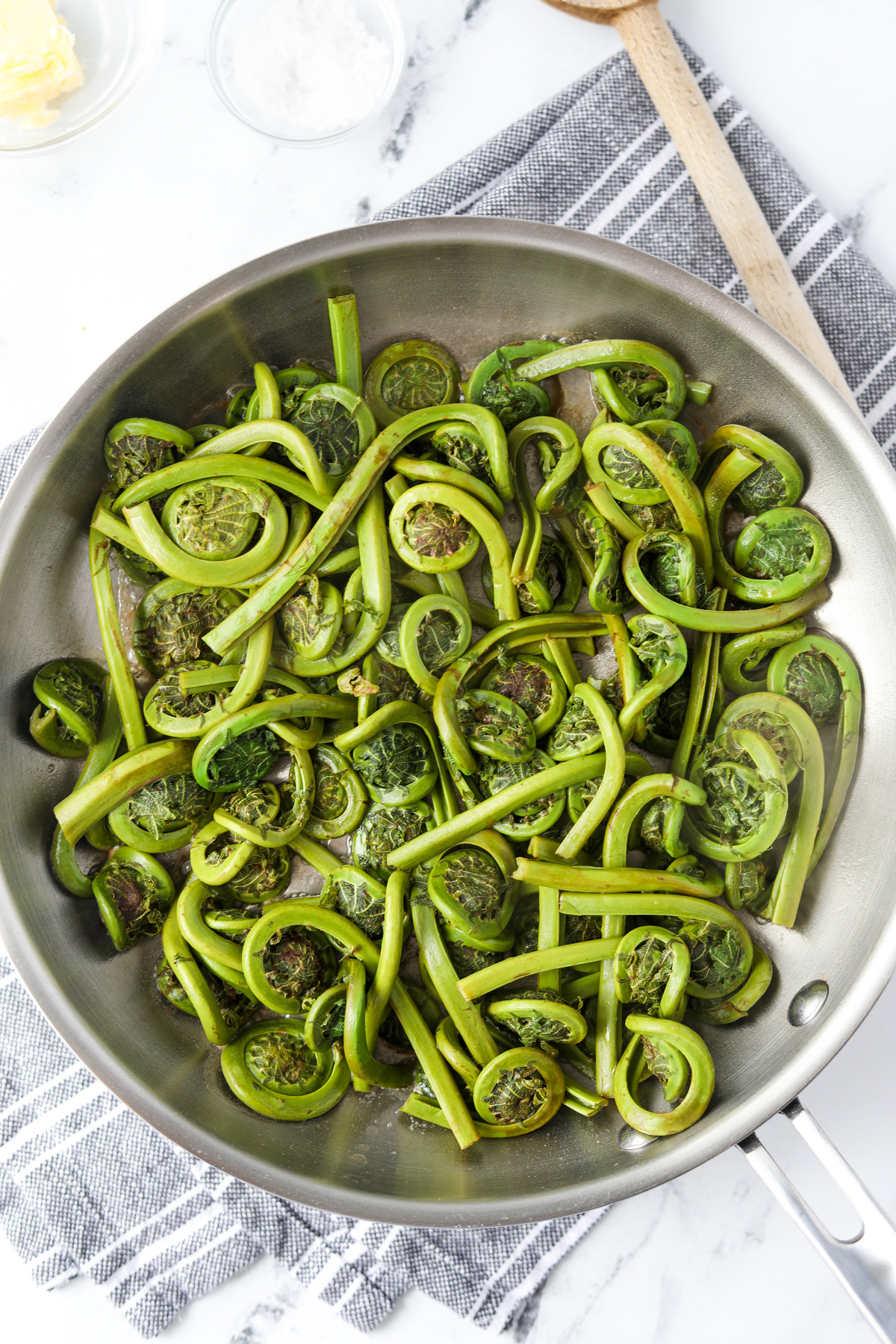 A skillet with cooked fiddleheads inside.