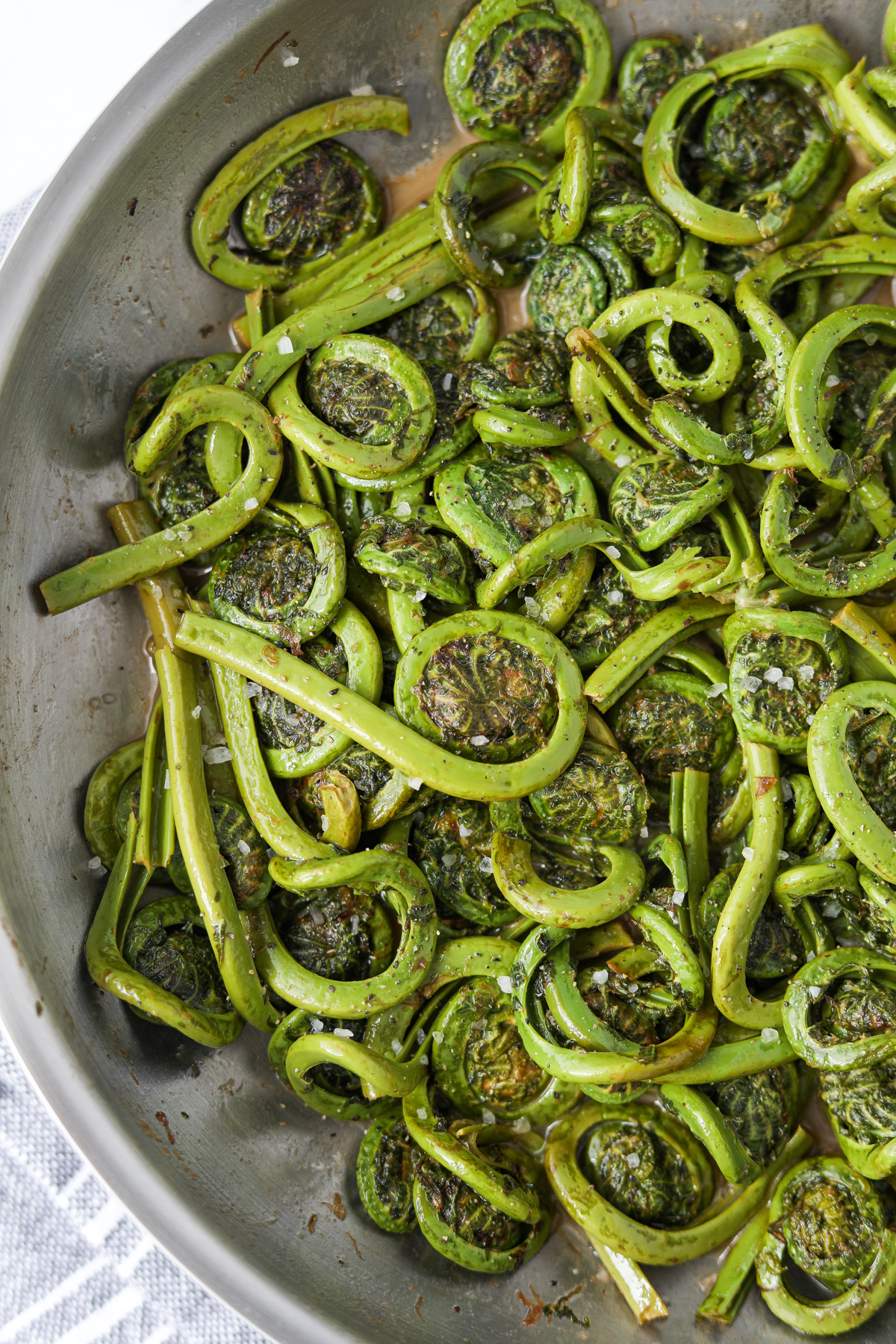 A skillet with fiddleheads that have been sauteed until lightly browned.