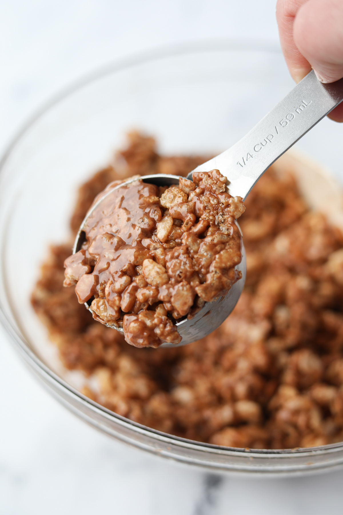 Scooping chocolate coated Rice Krispies with a measuring cup.