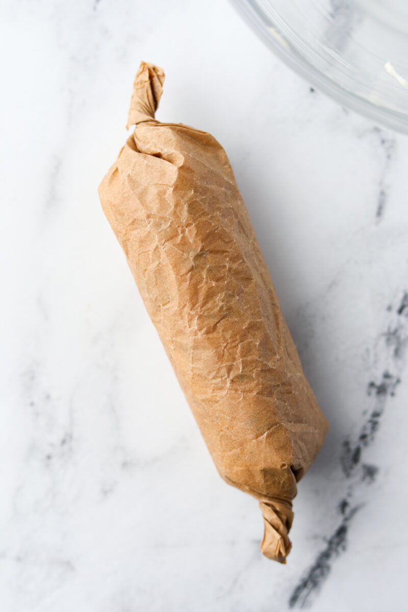 A log of butter wrapped up in brown parchment paper.