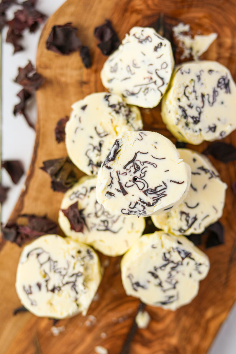 A stack of round compound butter slices dotted with dulse (seaweed).