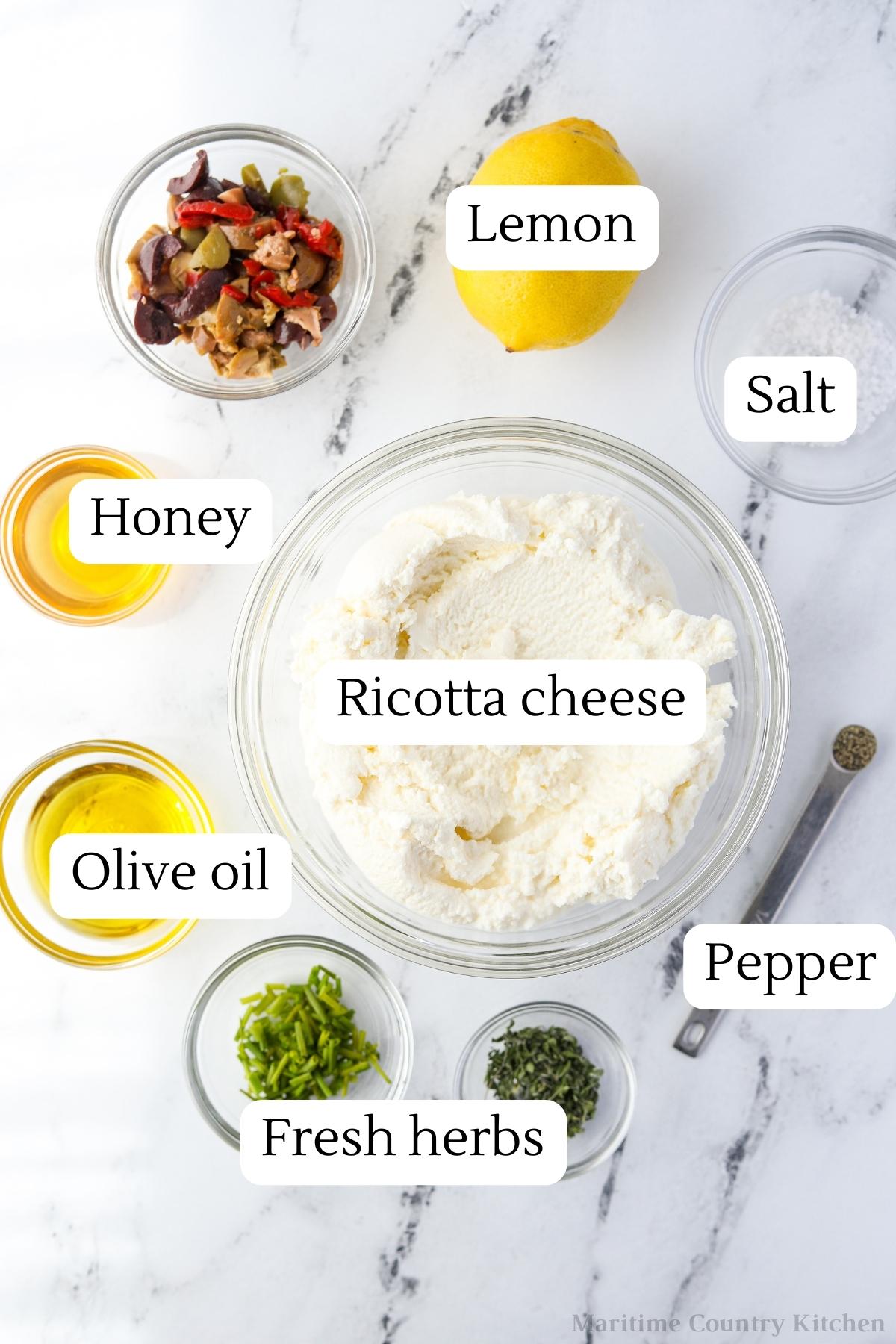 The ingredients needed to make whipped ricotta: ricotta cheese, olive oil, lemon, fresh herbs, salt, pepper, etc.