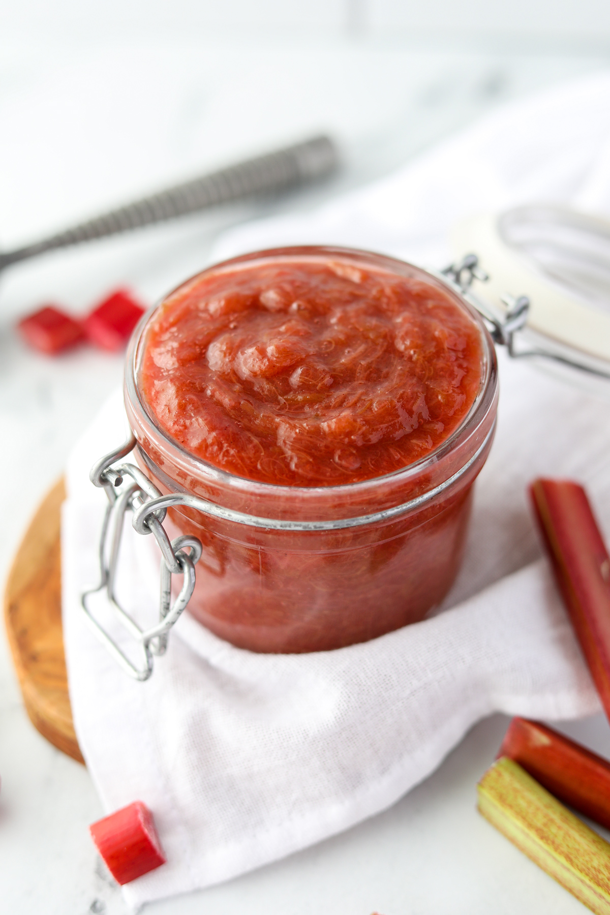 A small jar filled with rhubarb sauce resting on a wood board.