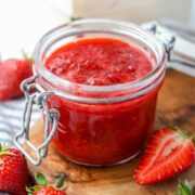 A small jar of fruit compote, with fresh strawberries spread around next to it.
