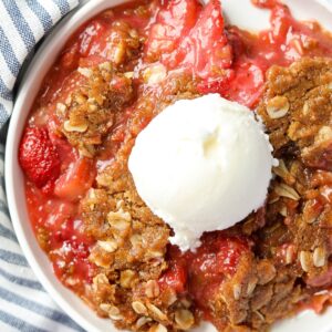 A serving of strawberry rhubarb crisp topped with a scoop of vanilla ice cream.