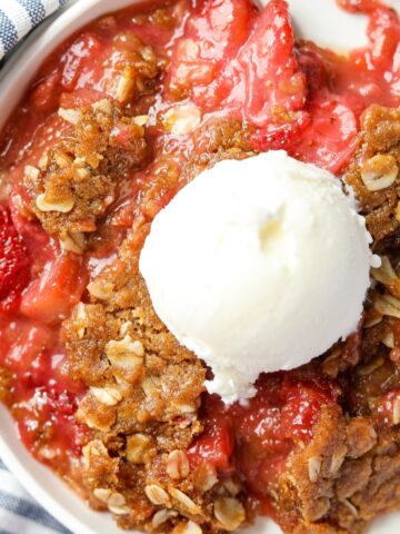 A serving of strawberry rhubarb crisp topped with a scoop of vanilla ice cream.
