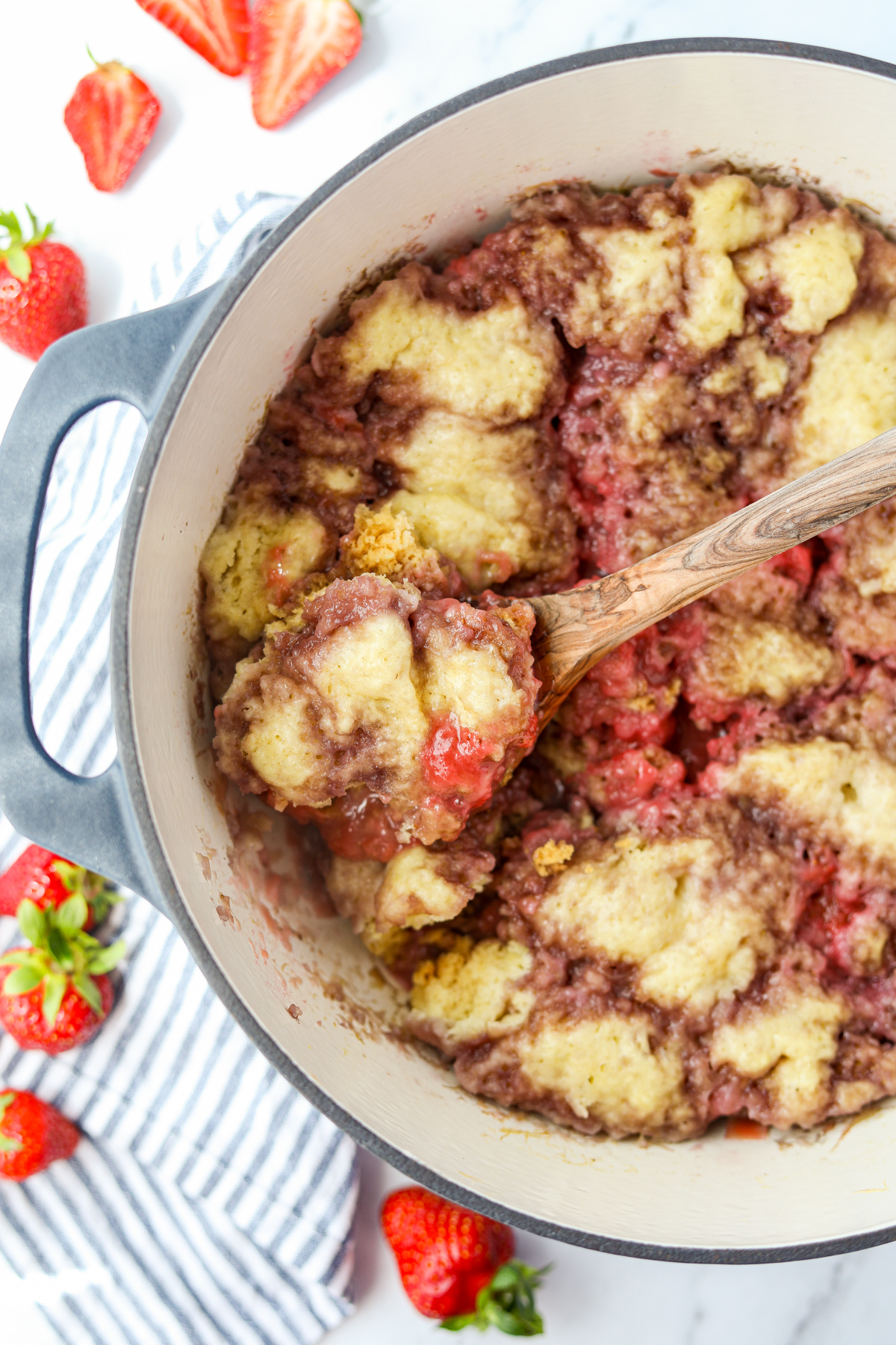 A Dutch Oven filled with strawberry rhubarb grunt, with a spoon taking a portion out.
