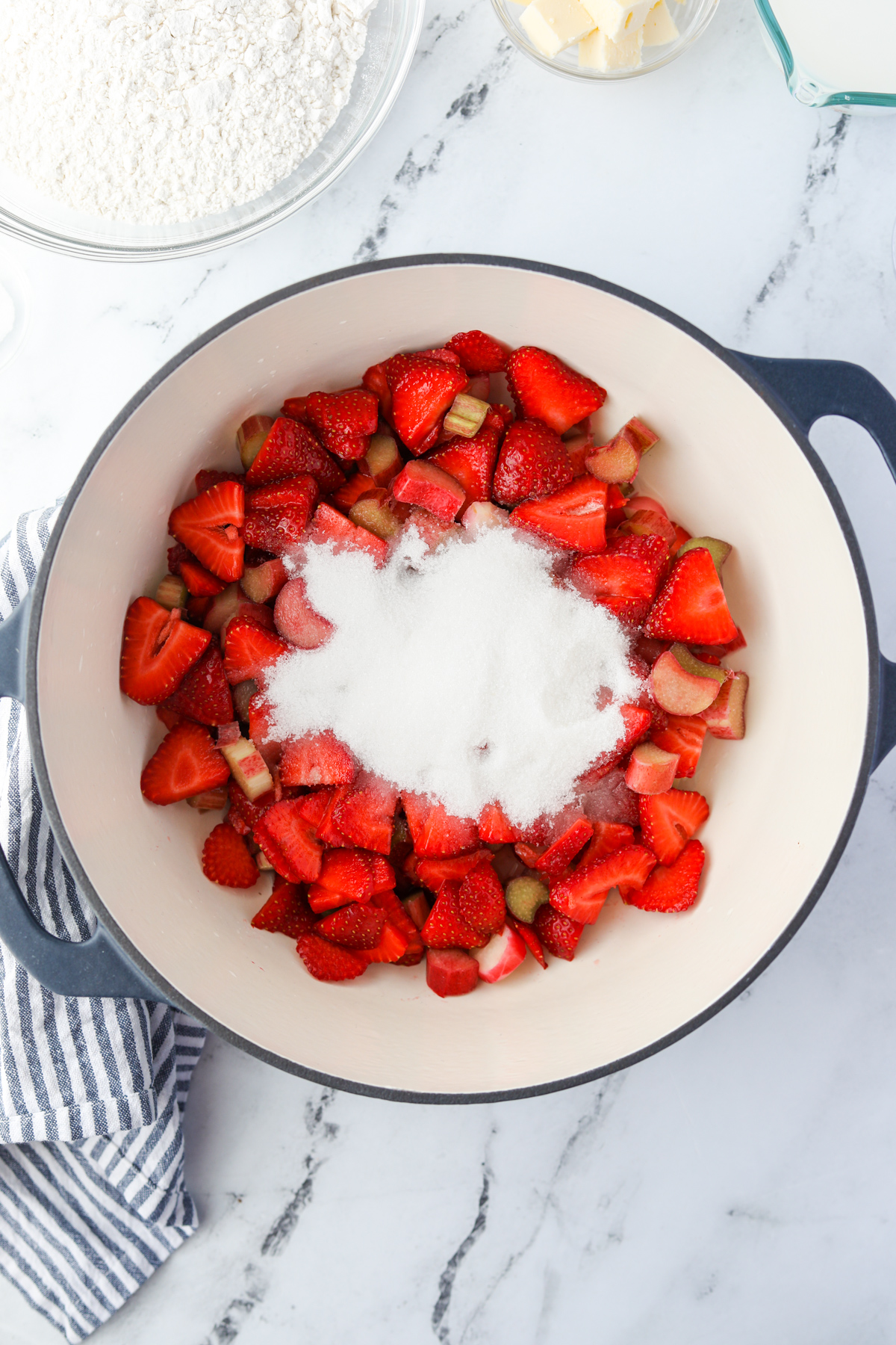 A Dutch Oven filled with strawberries, rhubarb, and white sugar.