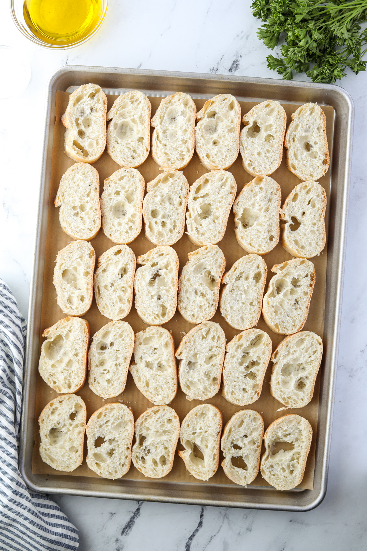 A baking sheet with slices of baguette lined up.