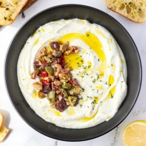 A bowl of whipped ricotta garnished with chopped olives, olive oil, and fresh thyme.