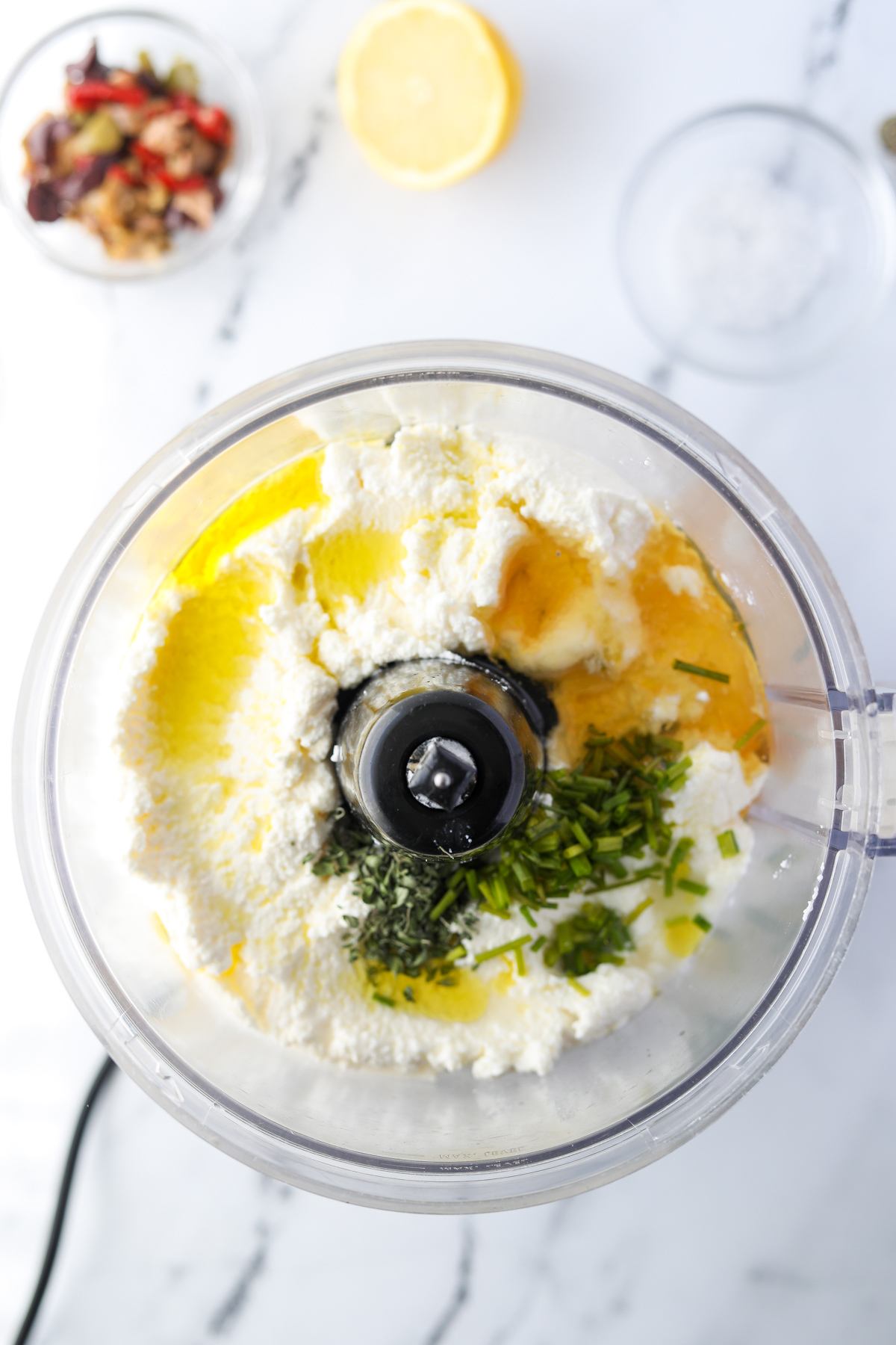 A food processor filled with ricotta, lemon, honey, herbs, and olive oil.