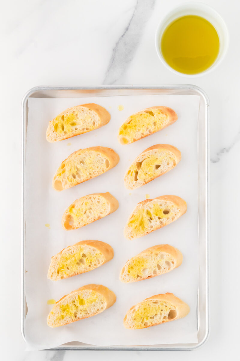 A baking sheet with baguette slices on it, brushed with oil.