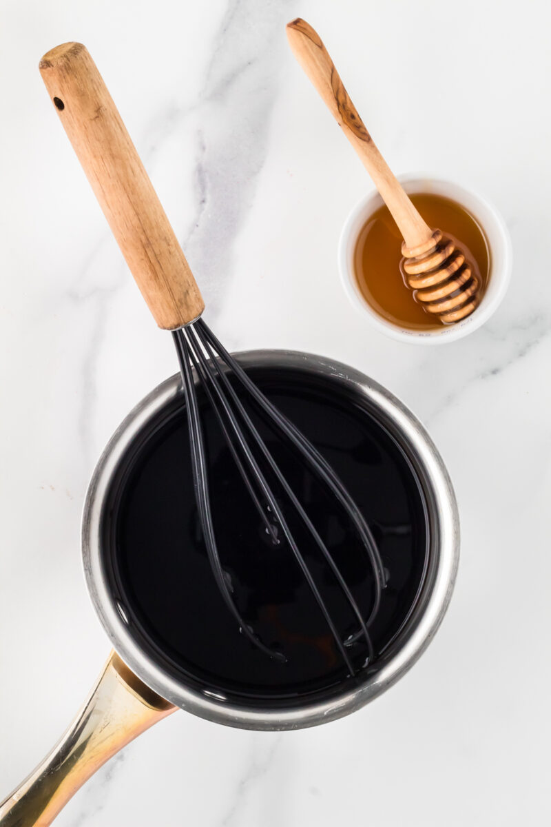 A small saucepan filled with balsamic vinegar, with a small bowl of honey next to it.
