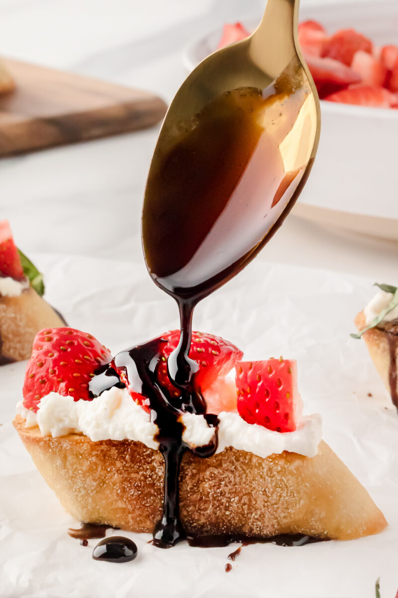 Drizzling a strawberry ricotta crostini with balsamic glaze from a spoon.