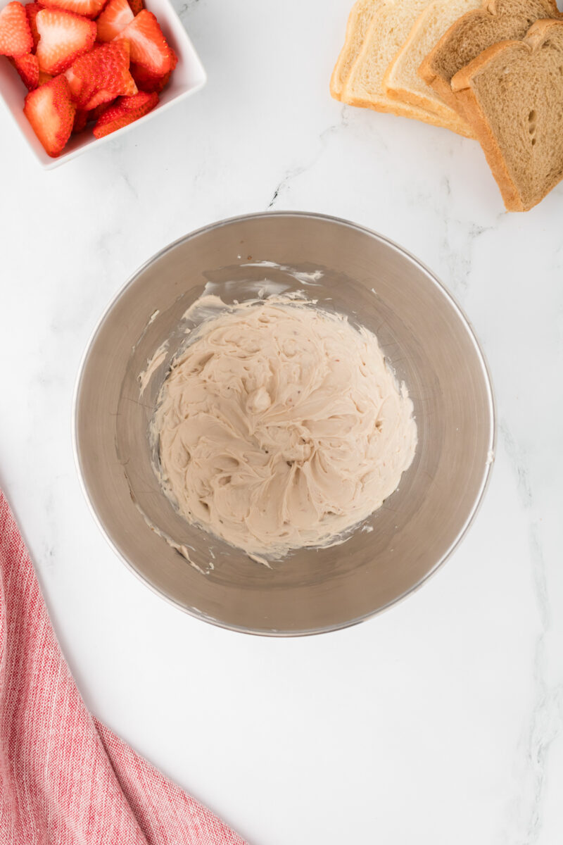 A stand mixer bowl with whipped cream cheese inside.