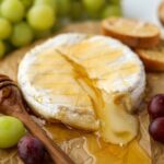 A wheel of brie cheese topped with honey and surrounded by grapes.