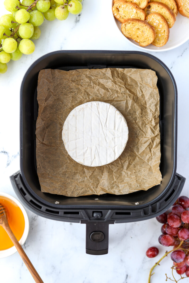 A wheel of cheese in an air fryer lined with parchment paper.