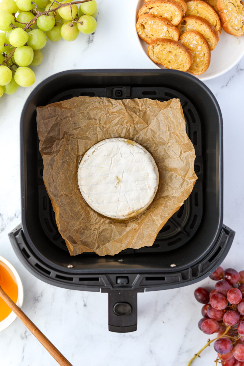 A wheel of brie cheese inside of a parchment-lined air fryer basket.
