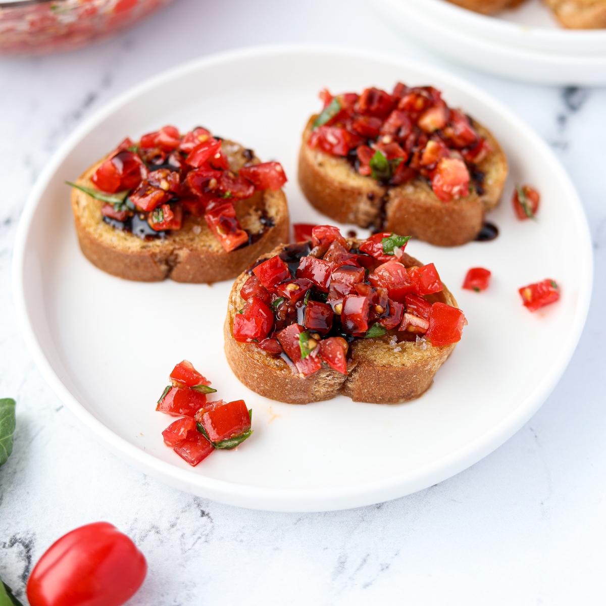 Three mini tomato toasts on a white plate garnished with balsamic glaze.