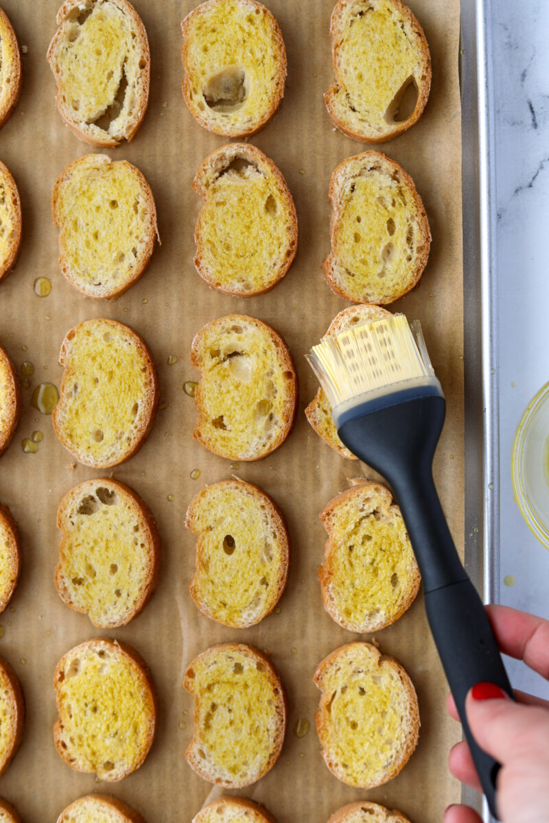 Brushing baguette slices with olive oil.