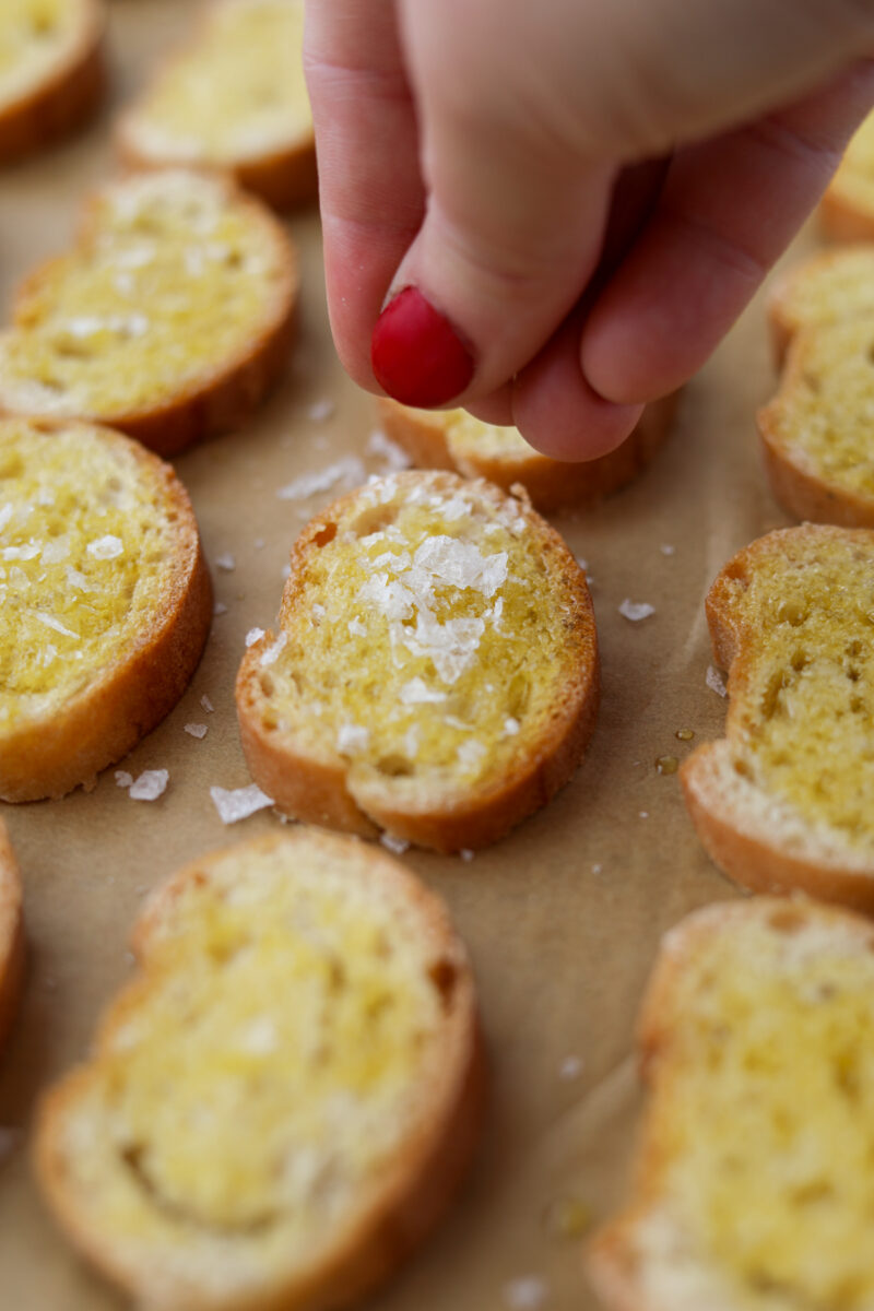 Sprinkling salt on a mini baguette slice.
