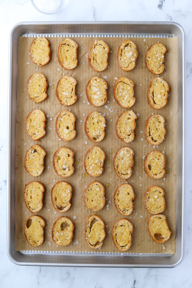 A baking sheet filled with lightly toasted baguette rounds.