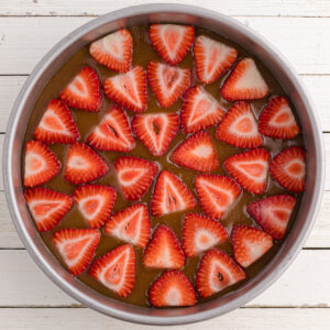 Adding strawberries in an even layer on top of brown sugar in a cake pan.