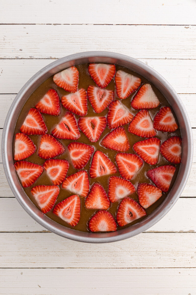 Adding strawberries in an even layer on top of brown sugar in a cake pan.