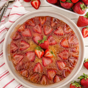 A strawberry upside down cake on a cake platter, garnished with fresh strawberries.