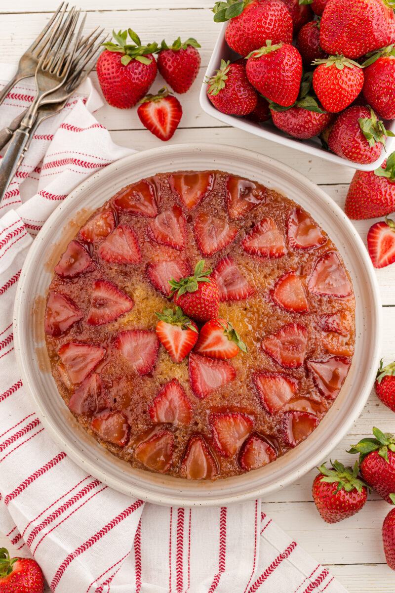 A strawberry upside down cake on a cake platter, garnished with fresh strawberries.