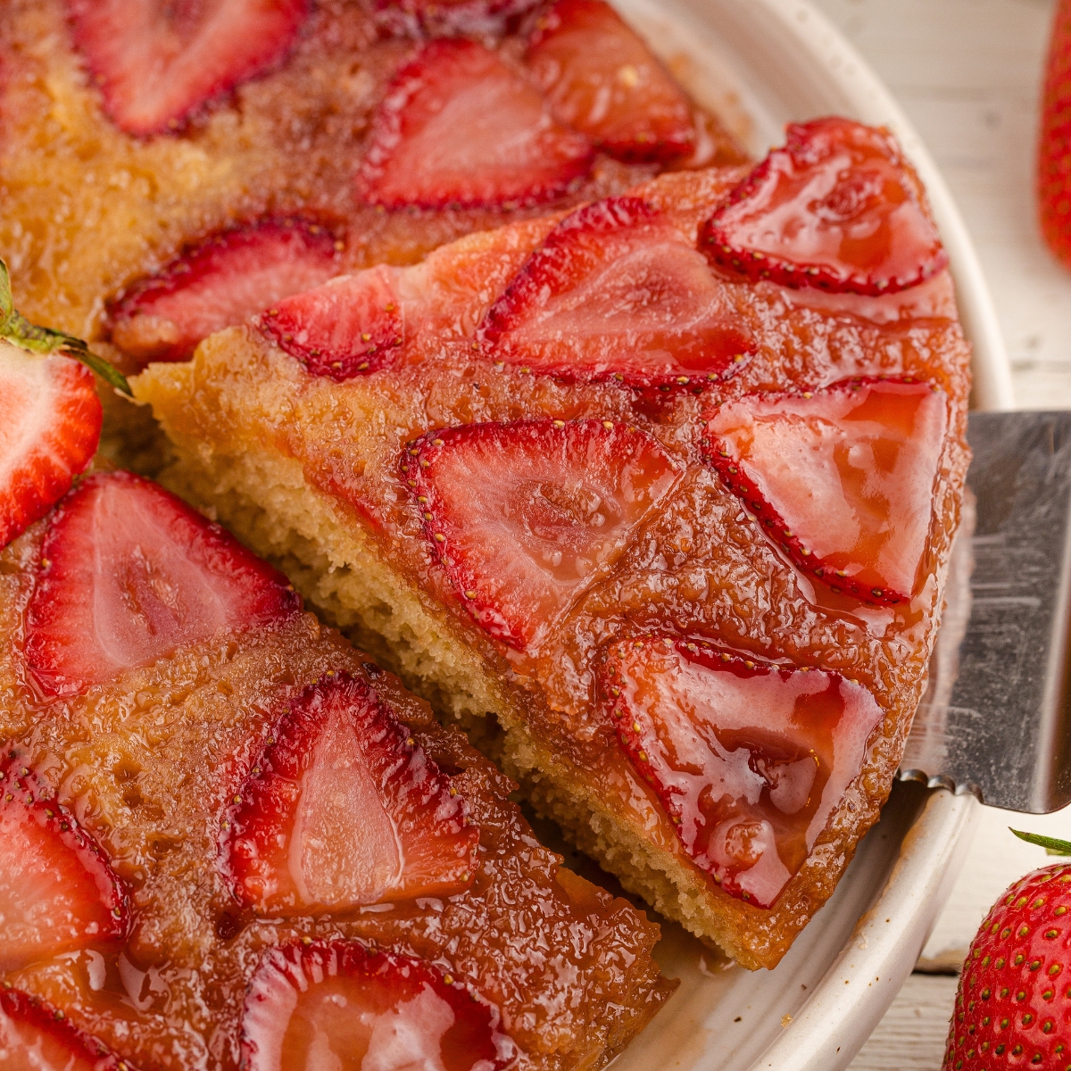 A cake lifter taking a slice of strawberry cake from a serving platter.
